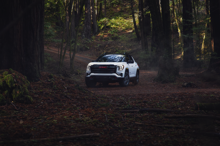 2026 GMC Terrain compact SUV driving on a wooded trail, showing its off-road capability and all-wheel-drive performance.