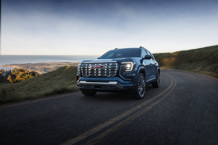 2026 GMC Terrain compact SUV driving on a scenic road with hills and coastline in the background.