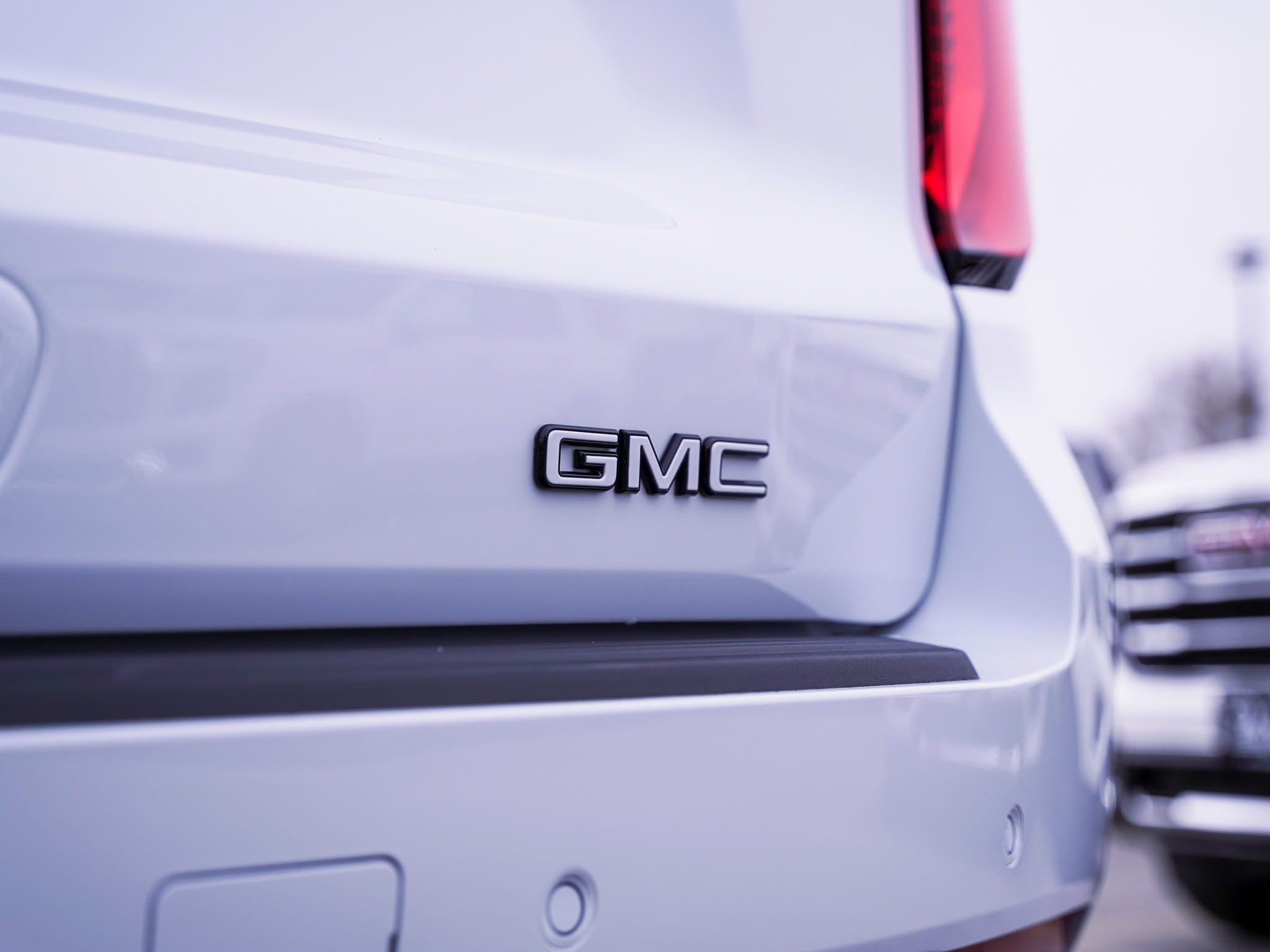 Detail shot of the white and black GMC rear badge on a custom 2026 GMC Yukon Denali with Glacier White Tricoat paint and chrome delete